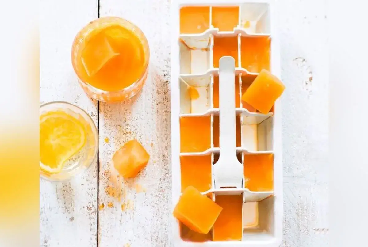Glaçons orange vif dans un bac à glaçons, prêts pour une recette spritz rafraîchissante. Un verre avec des glaçons et une tranche d'orange à côté.