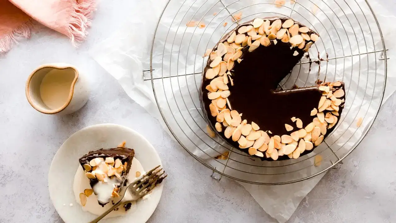 Un délicieux gâteau viennois au chocolat, garni d'amandes effilées, avec une part servie sur une assiette et un petit pichet de crème.