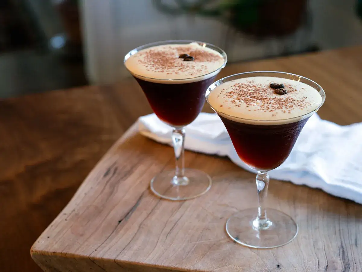 Deux verres de cocktail du moment, ornés de grains de café et de cacao, sur une planche en bois.