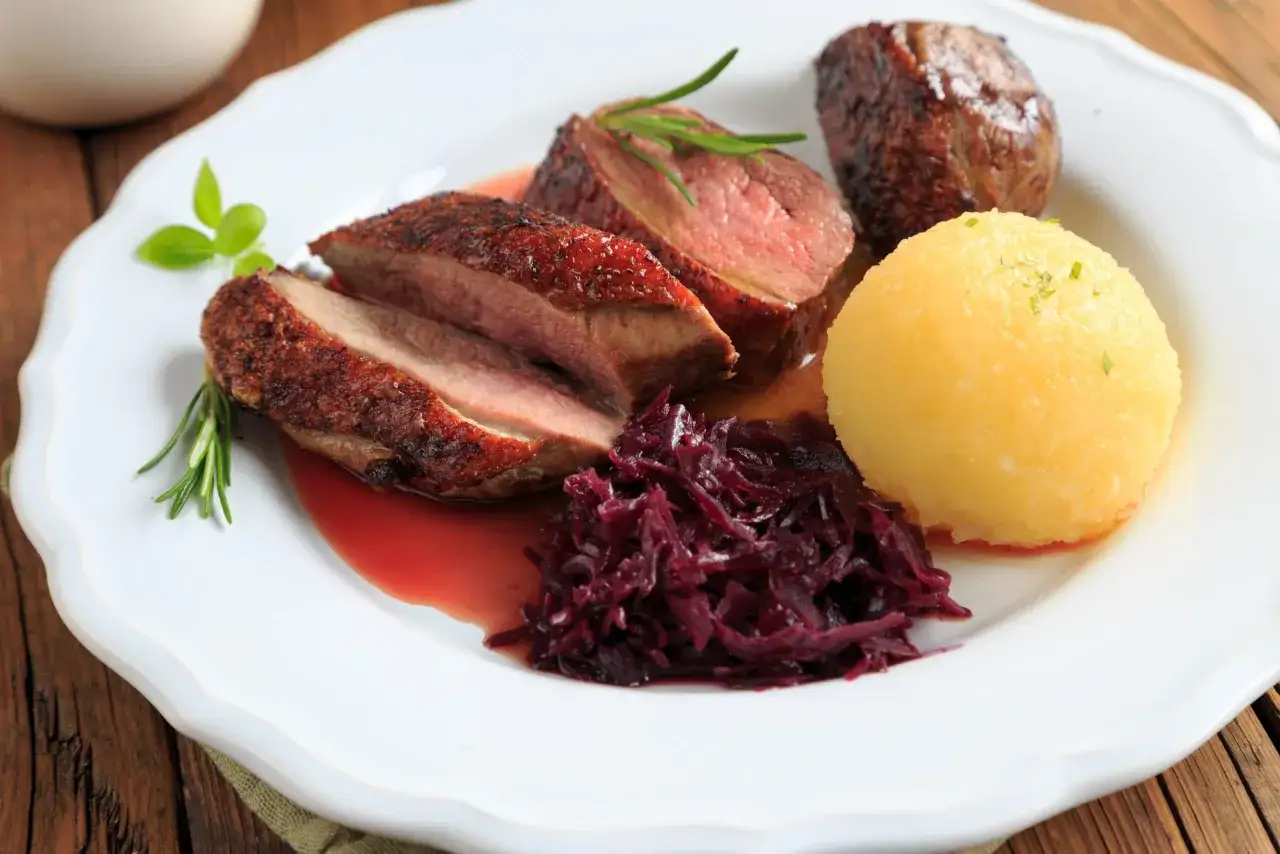 Magret de canard tranché, servi avec chou rouge et une quenelle. Un plat savoureux, parfait pour se demander que boire avec du magret de canard.