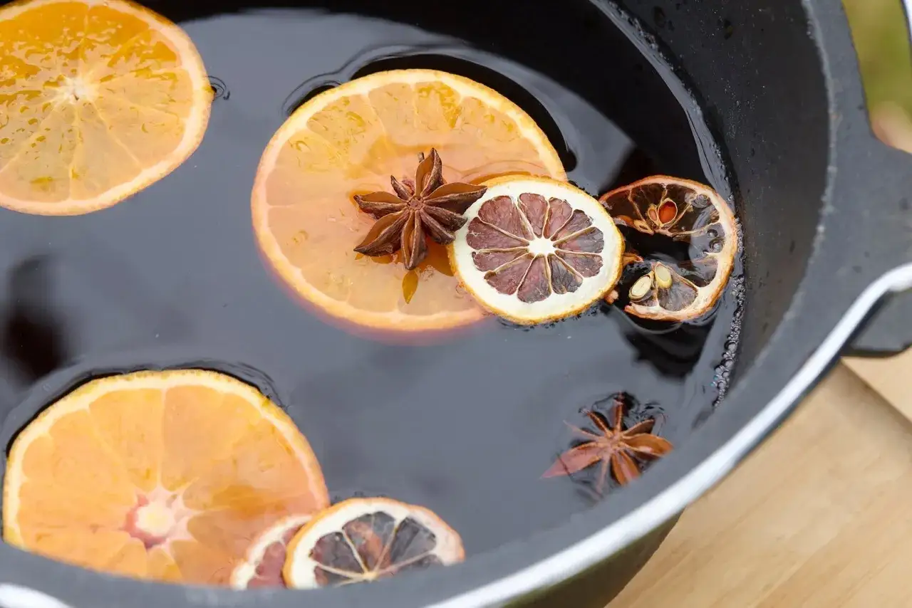 Tranches d'orange et d'orange séchée, avec des étoiles de badiane, flottant dans un liquide sombre, prêtes pour une recette de vin chaud.