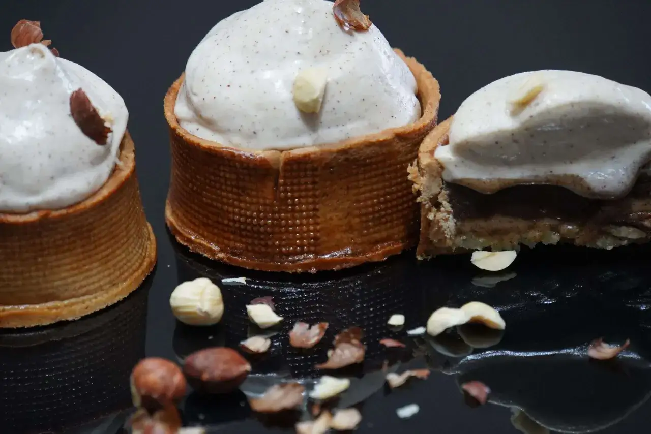 Trois tartelettes garnies d'une mousse légère et parsemées de noisettes concassées. Le praliné noisette est subtilement présent.