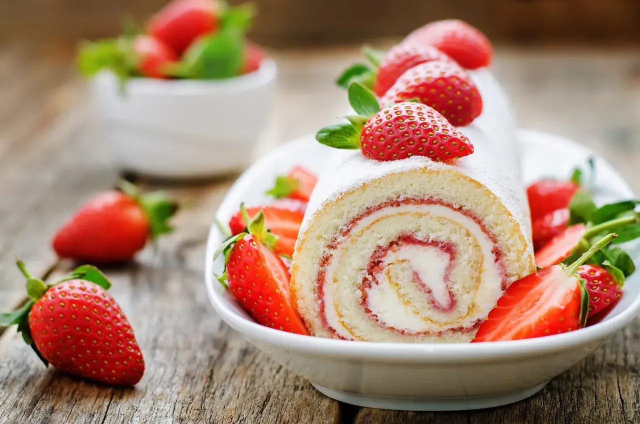 Un délicieux biscuit roulé moelleux garni de crème et de fraises, saupoudré de sucre glace.