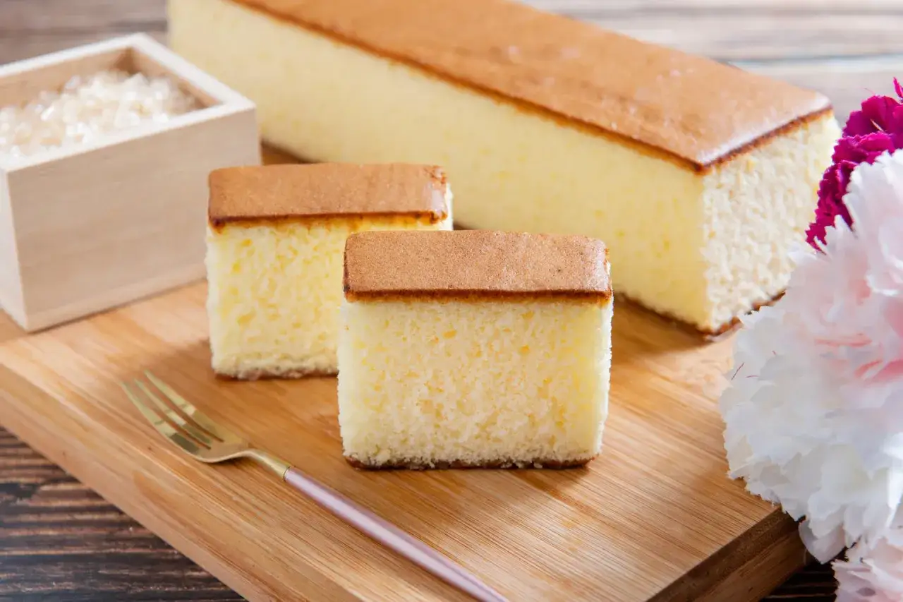 Délicieux gateau japonais, moelleux et aérien, coupé en tranches sur une planche en bois, avec une petite fourchette dorée et des fleurs.
