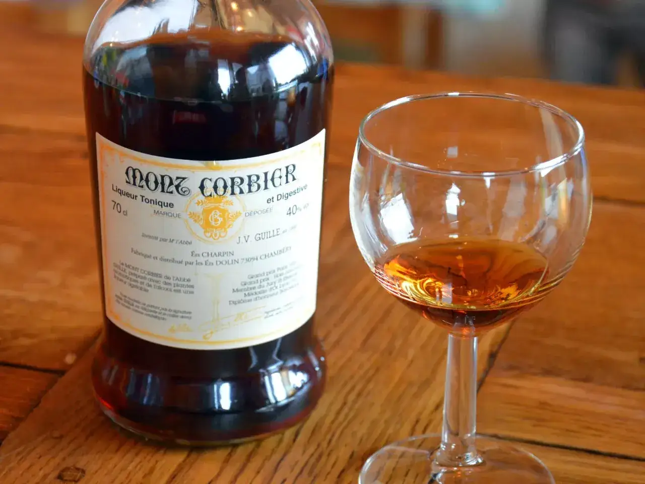 Une bouteille de Mont Corbier, liqueur tonique et digestive, à côté d'un verre rempli de ce digestif alcool.