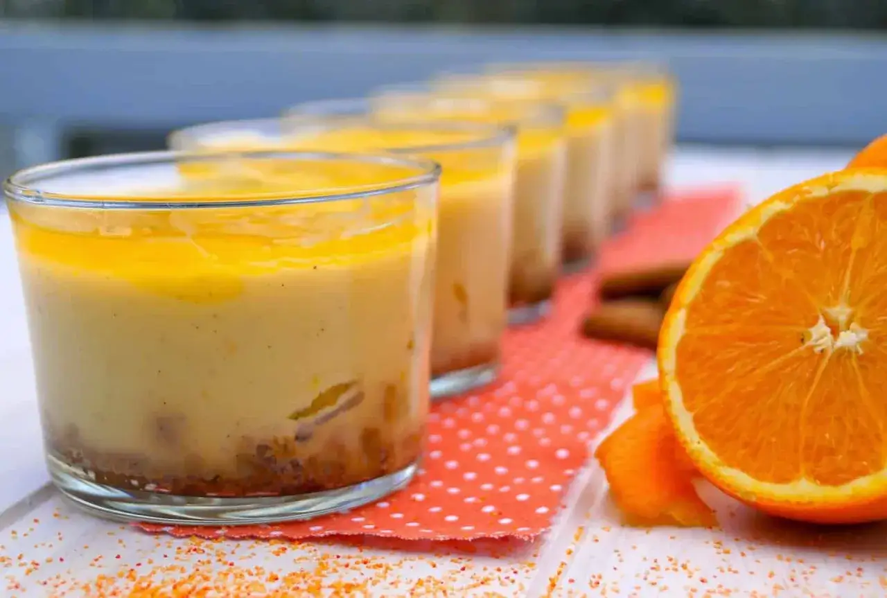 Petits verres de dessert crémeux, surmontés d'un coulis orange vif. Une tranche d'orange et des bâtonnets de cannelle complètent cette gourmandise.