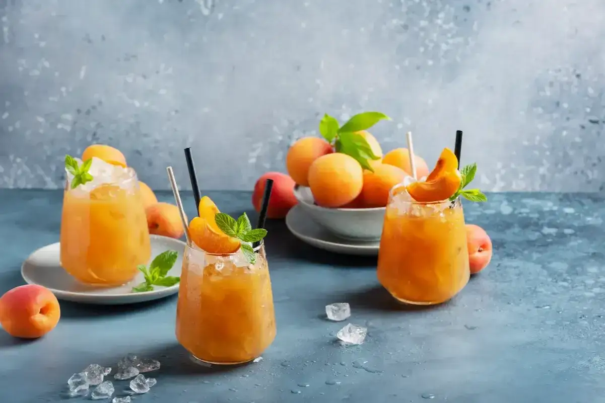 Trois cocktails rafraîchissants au jus d'abricot alcool, garnis de menthe et de quartiers d'abricot, sur un fond bleu texturé.
