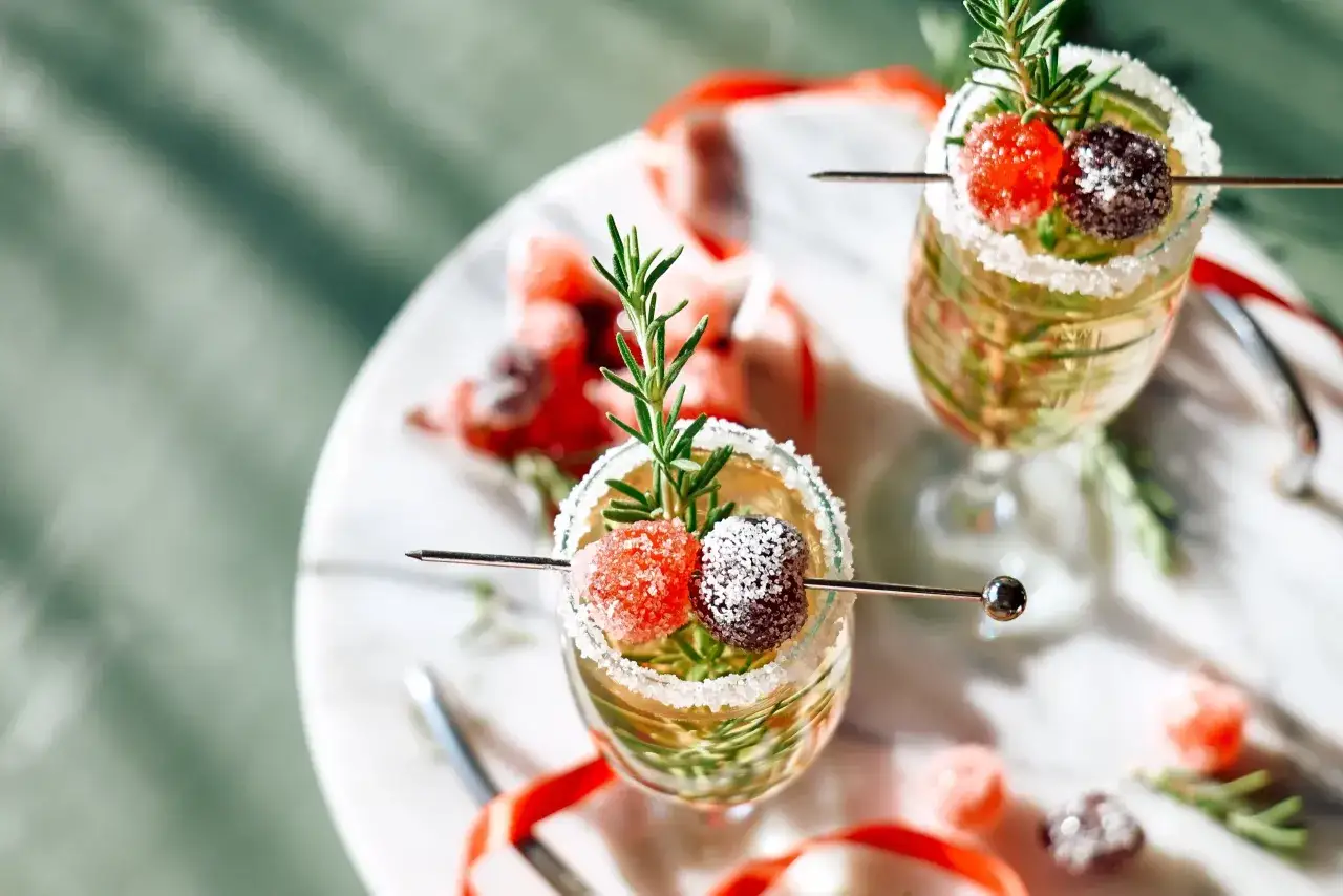 Un cocktail de Noël facile et rapide, décoré de romarin et de fruits confits givrés. Parfait pour les fêtes !