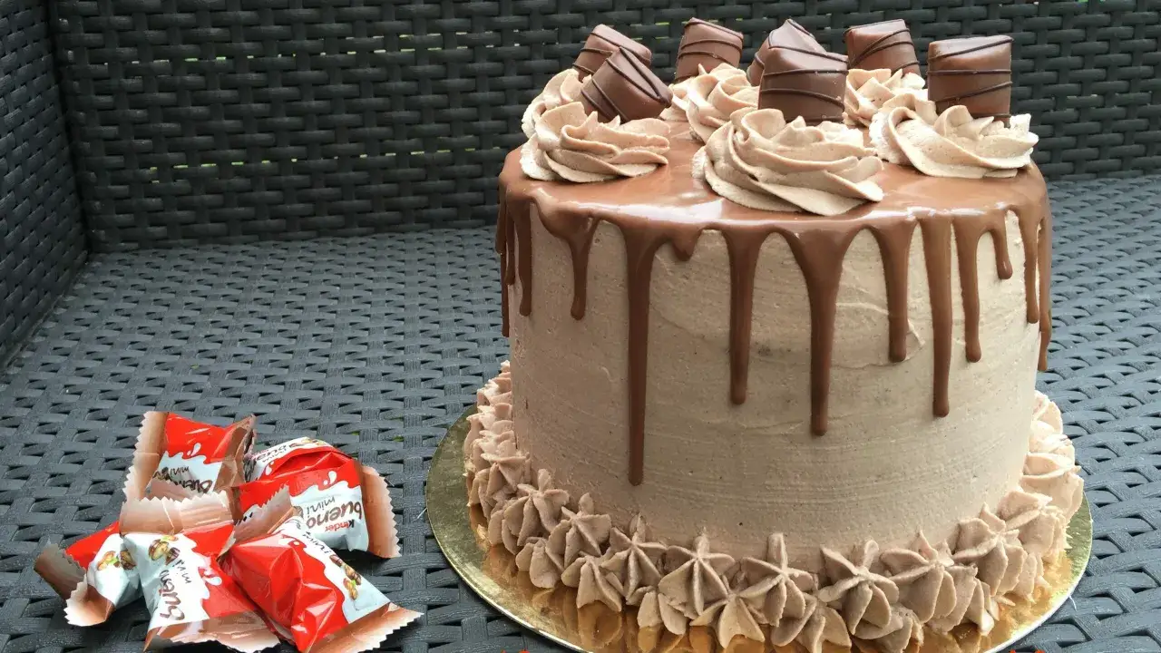 Gâteau au chocolat avec ganache et morceaux de Kinder Bueno, décoré de crème au beurre et de gouttes de chocolat.
