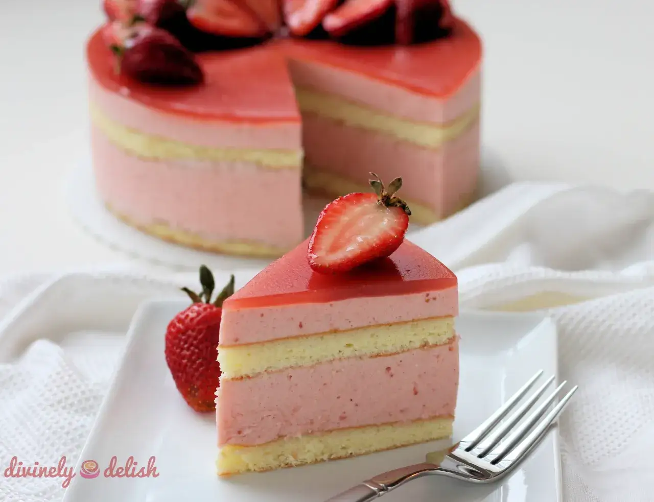 Tranche de gâteau rose à la ganache fraise, garnie de fruits frais. Un délice visuel et gustatif.