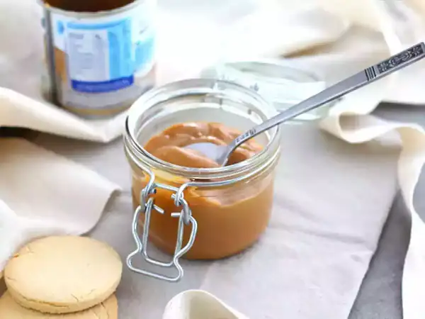 Un pot de confiture de lait onctueuse, une cuillère décorée et des biscuits sablés, prêts à être dégustés.
