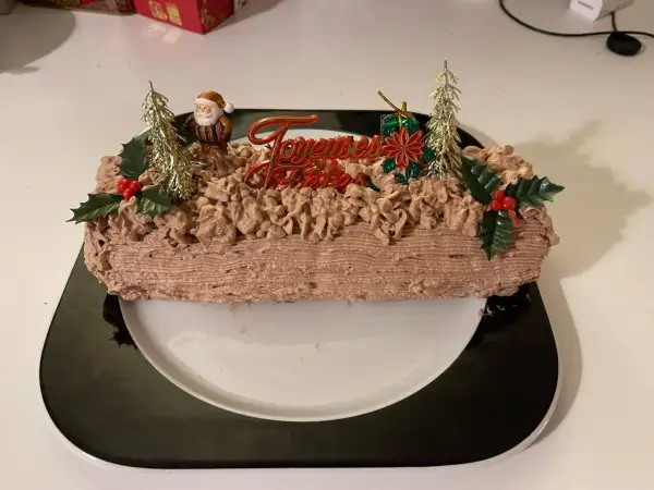 Bûche de Noël au chocolat, décorée de chantilly mascarpone, d'un Père Noël et de sapins dorés.