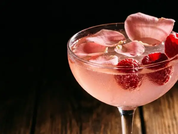 Cocktail rosé rafraîchissant garni de framboises et de pétales de rose. Une recette délicieuse pour l'été.