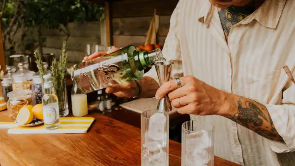 Un barman prépare un cocktail, versant du gin alcool de quoi dans un verre rempli de glaçons.