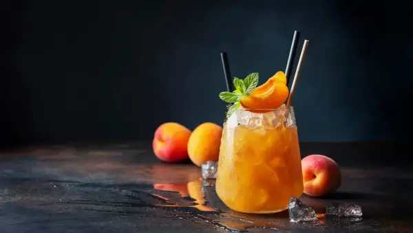 Un cocktail rafraîchissant au jus d'abricot alcool, garni d'une tranche d'abricot et de menthe, sur un lit de glace pilée.
