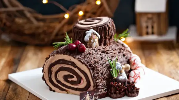 Bûche de Noël chocolatée, parfaite pour une recette génoise bûche moelleuse. Décorée de baies, romarin et d'une mini maison.