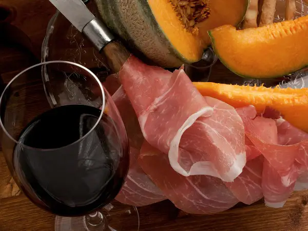 Un verre de vin rouge, du melon et du jambon cru. Quel vin avec melon et jambon cru ? Une belle association pour un apéritif gourmand.