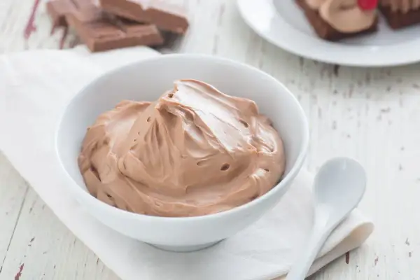 Un bol de namelaka chocolat onctueux, prêt à être dégusté. Des morceaux de chocolat sont visibles en arrière-plan.