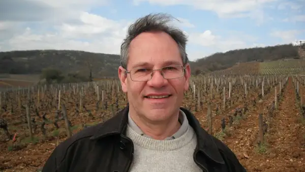 Alain Gras, souriant, se tient devant un vignoble vallonné.