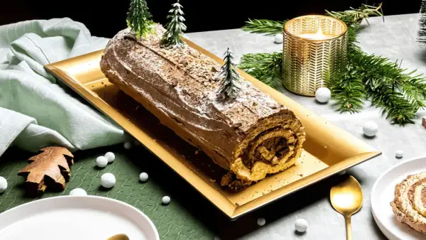 Une délicieuse recette de buche de Noel au chocolat, décorée de sapins miniatures et de neige, prête à être dégustée.