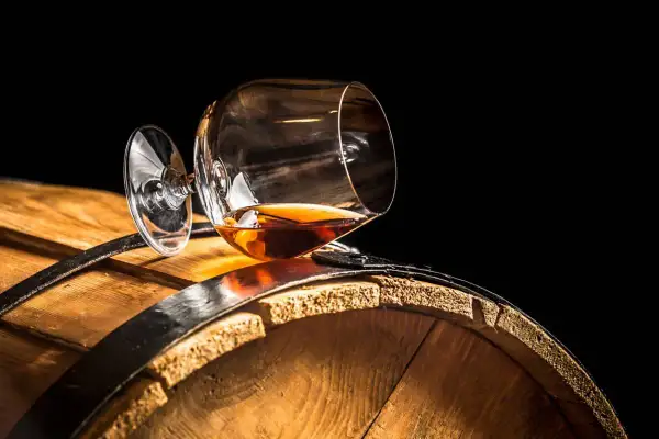 Verre de cognac renversé sur un tonneau en bois. Le liquide ambré suggère une question : le vin est-il un spiritueux ?
