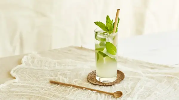 Un verre de nom de cocktail rafraîchissant avec de la menthe et de la glace, sur une nappe en dentelle.