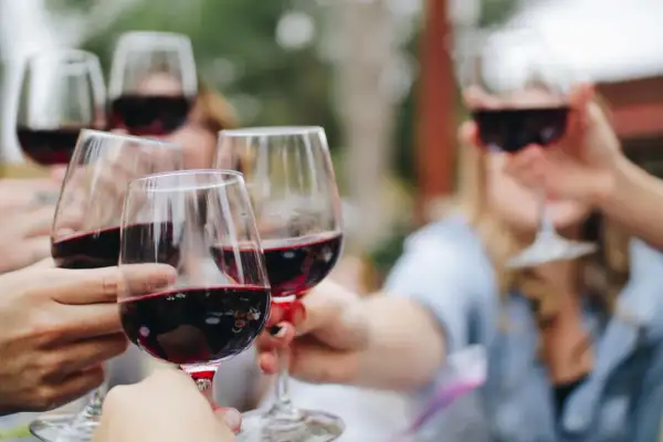 Des mains lèvent des verres de vin rouge pour un apéritif convivial.
