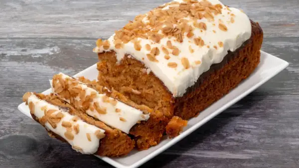 Un délicieux gâteau carotte, généreusement glacé et parsemé de noix croquantes, est servi sur une assiette blanche.