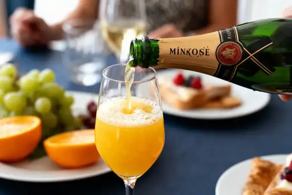 Une bouteille de Mimosé verse son contenu pétillant dans un verre rempli de jus d'orange, créant un cocktail mimosa parfait pour un brunch.