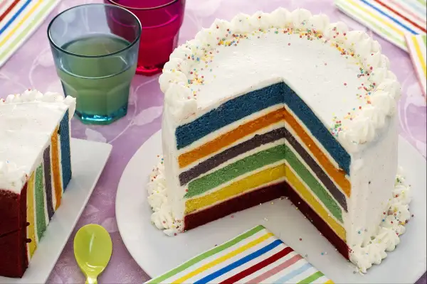 Un gâteau arc en ciel aux couches colorées, décoré de crème et de vermicelles, prêt à être dégusté.