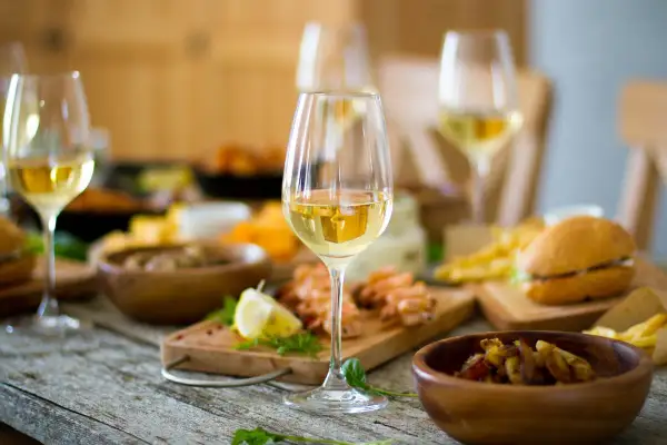 Verre de bordeaux blanc moelleux, parfait accompagnement pour crevettes, frites et mini-burgers sur une table rustique.