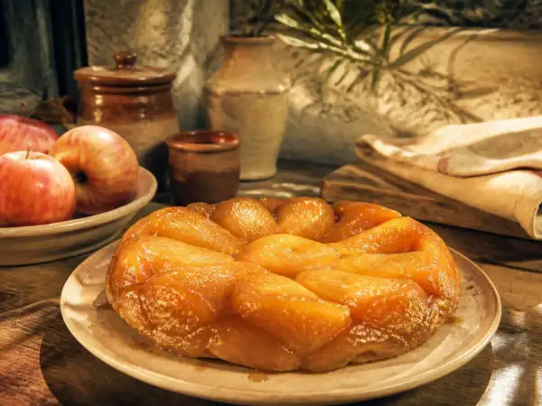 Une tarte tatin inratable, dorée et caramélisée, prête à être dégustée. Des pommes fraîches l'accompagnent.