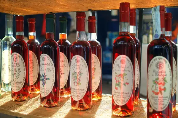 Plusieurs bouteilles de ratafia aux fruits rouges, dont le ratafia aux cerises et aux mûres, sont alignées sur une étagère en osier.