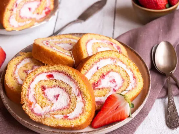Tranches de gâteau roulé aux fraises et à la crème, parfaites pour une recette gâteau roulé facile. Une fraise coupée est posée sur l'assiette.