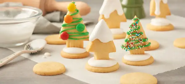 Biscuits en forme de sapins décorés de glaçage vert, vermicelles colorés et bonbons. Une recette festive à partager.