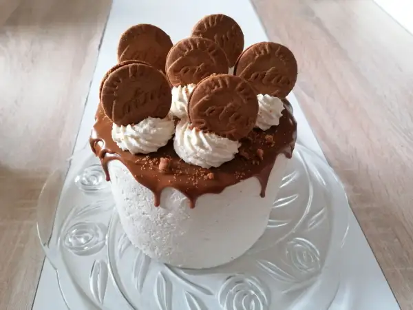 Gâteau blanc crémeux, nappé de chocolat fondant et décoré de biscuits spéculoos et de crème fouettée.