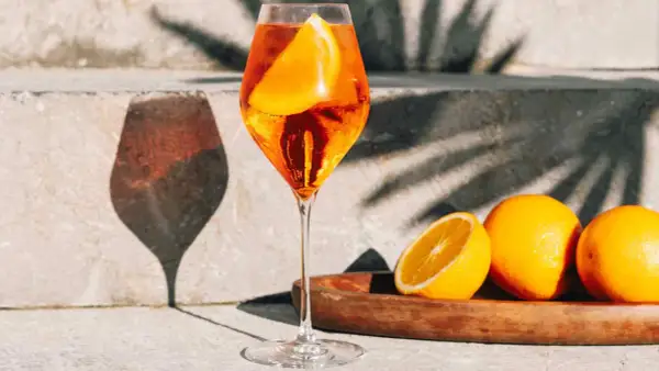 Un verre de Spritz pétillant, garni d'une tranche d'orange, avec des oranges fraîches sur un plateau. Parfait pour une recette spritz d'été.