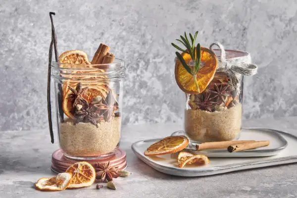 Ingrédients pour une recette de vin chaud : sucre, bâtons de cannelle, anis étoilé, cardamome, orange séchée et vanille dans des bocaux.