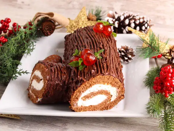 Un délicieux biscuit roulé moelleux au chocolat, décoré de cerises et de menthe, entouré de décorations de Noël.