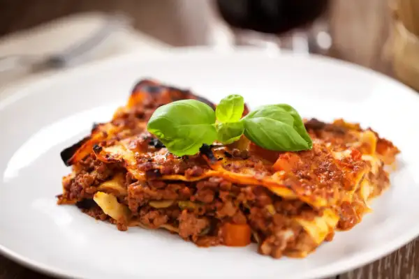 Une part de lasagne savoureuse, garnie de basilic frais, parfaite avec un verre de vin rouge.
