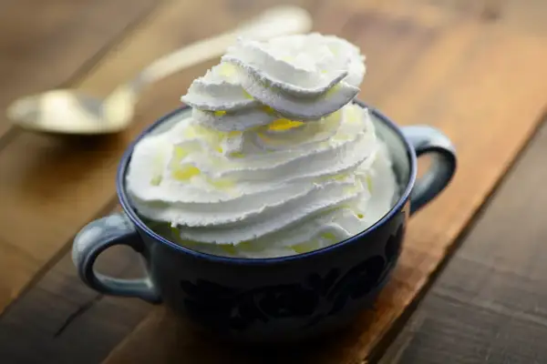 Une tasse de chantilly maison, aérienne et onctueuse, prête à être dégustée. Une cuillère dorée est posée à côté.