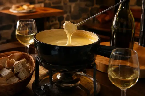 Une belle quantité de vin blanc accompagne une fondue savoyarde fumante, prête à être dégustée avec du pain croustillant.