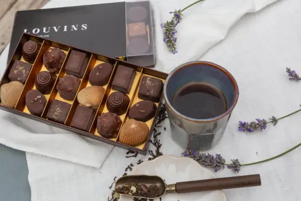 Boîte de chocolats Louvins, dont une ganache praliné, avec une tasse de café et des brins de lavande.